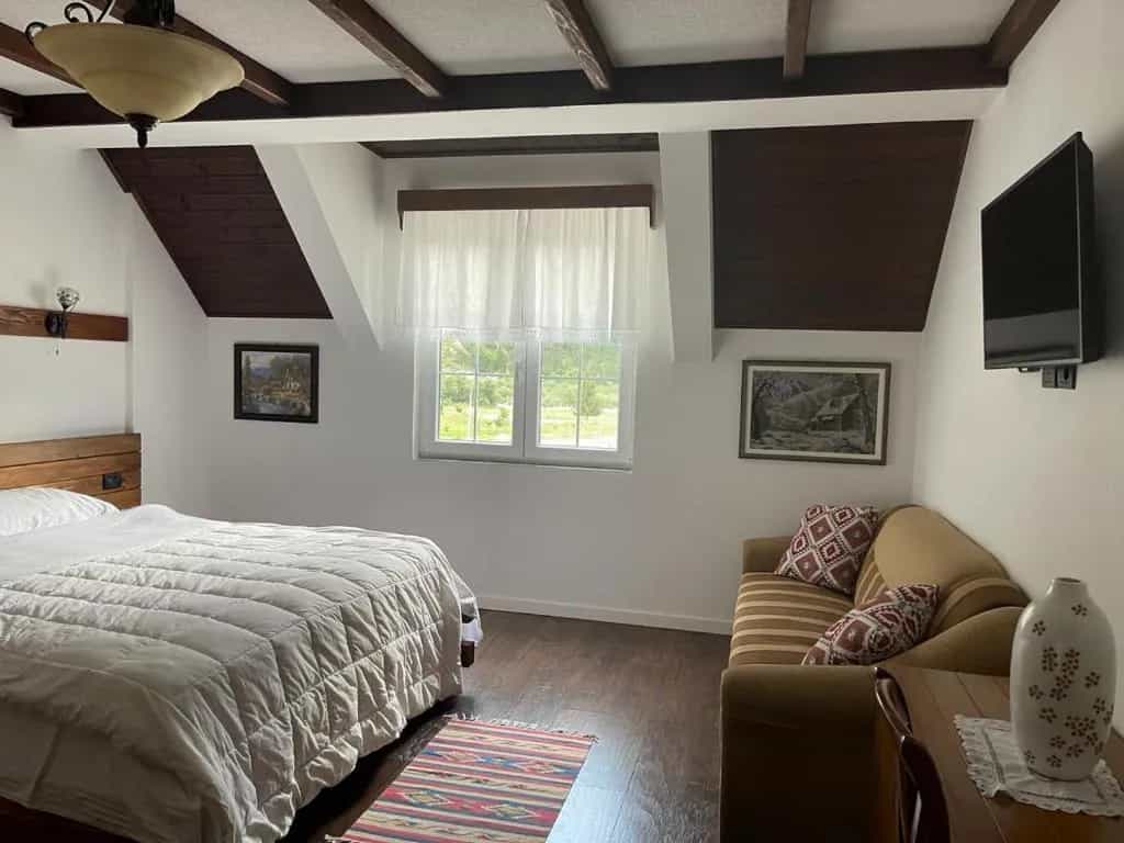Bedroom in BUJTINA Valbone with white bedding, wood beams, and a view of greenery.
