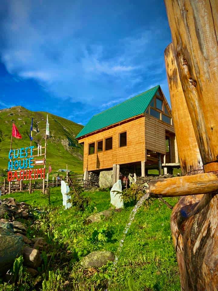 Guest House Bashkimi with green roof near grassy mountain under blue sky