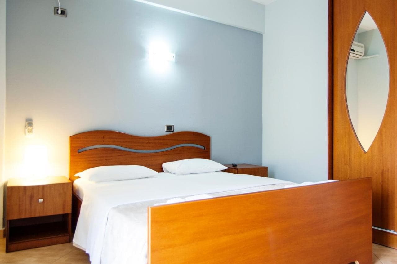 Double bed with white linens, wooden headboard, and bedside tables in a Dhima Hotel room in Himare.