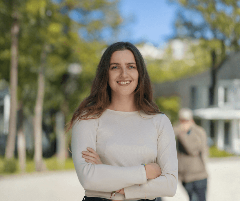 Smiling woman with arms crossed standing outdoors in a park setting.