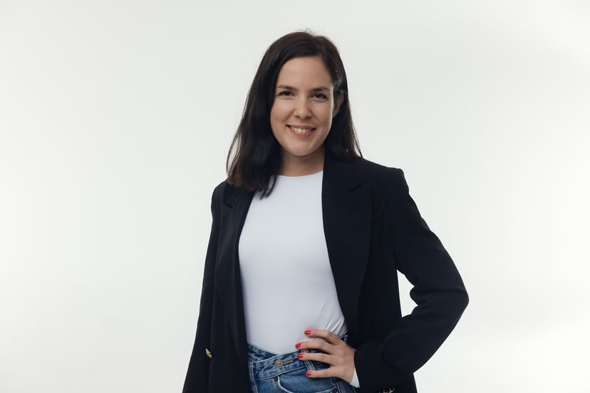 Woman with dark hair smiling while wearing a white t-shirt and black blazer against a white background.