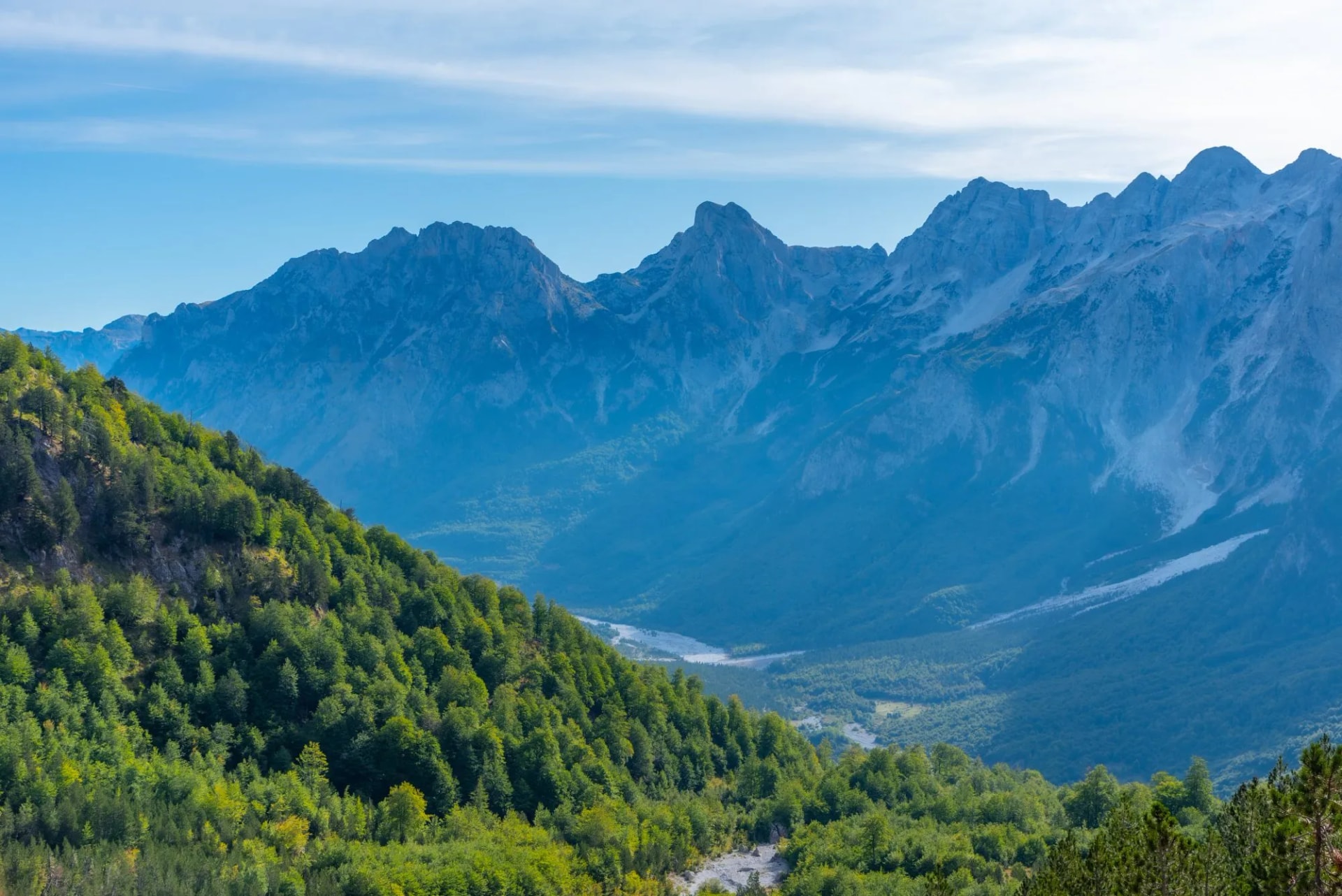 Aerial view of Valbona valley in Albania with lush green slopes and rugged blue mountains.