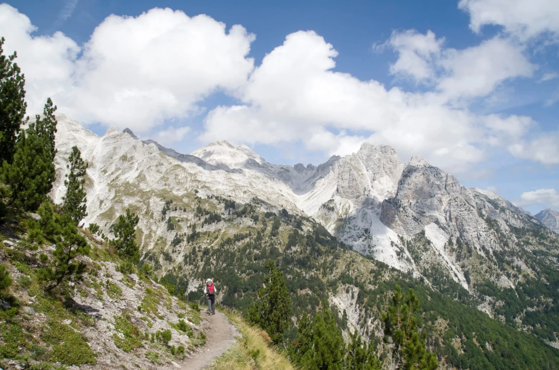 Hiker on trail viewing Jezerca summit in Albanian Alps from Valbona Pass.