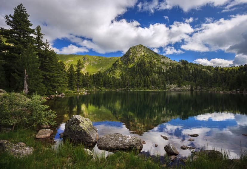 Serene view of Hridsko lake in Prokletije mountains National Park with reflections under a cloudy blue sky.