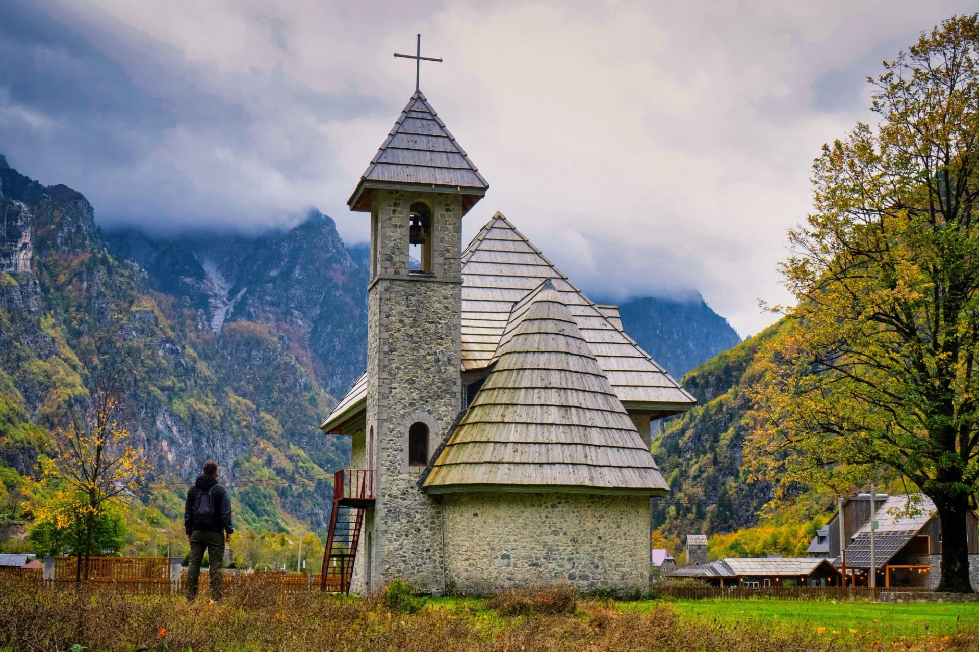 Stone church in Thethi National Park with autumn foliage and cloudy mountains.